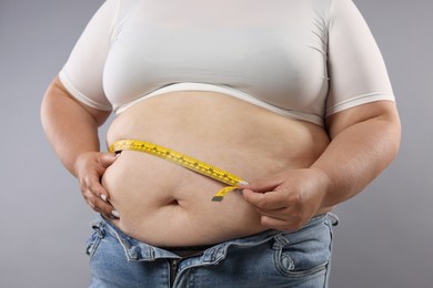 Photo of Overweight woman measuring her belly with tape on grey background, closeup