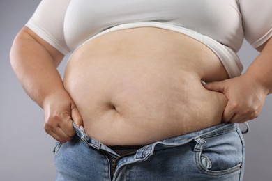 Photo of Woman with excessive belly fat on grey background, closeup. Overweight problem