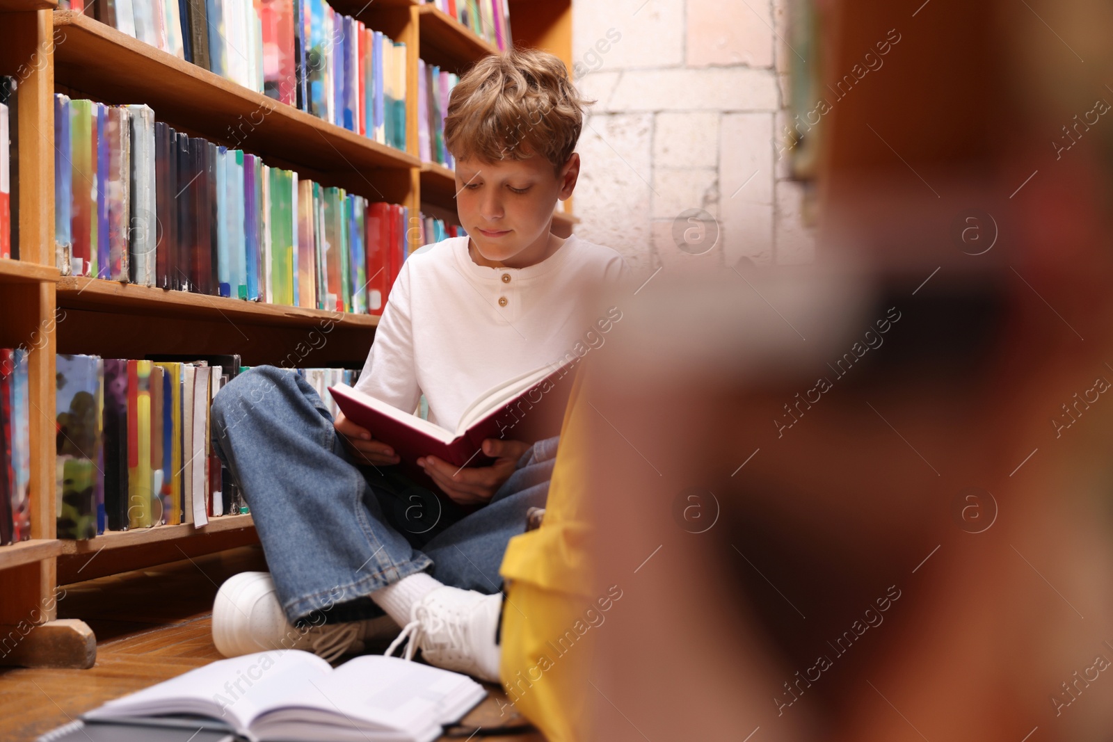 Student reading book on floor in library Photo of Student reading book on floor in library