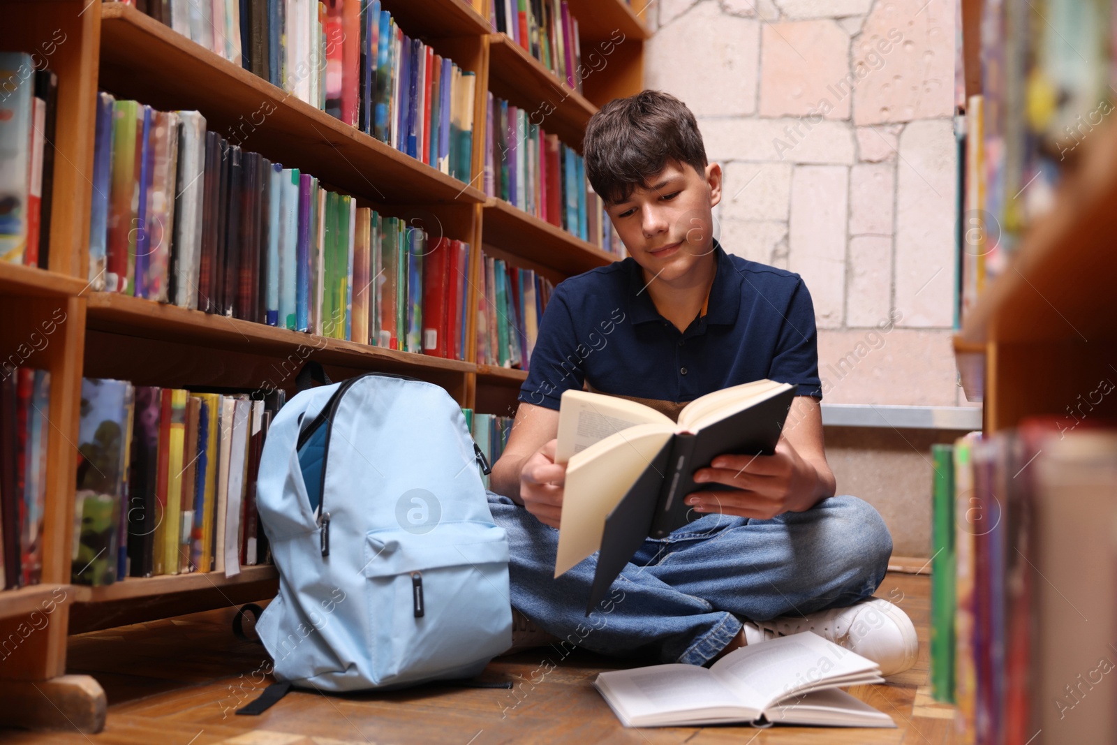 Student reading book on floor in library Photo of Student reading book on floor in library