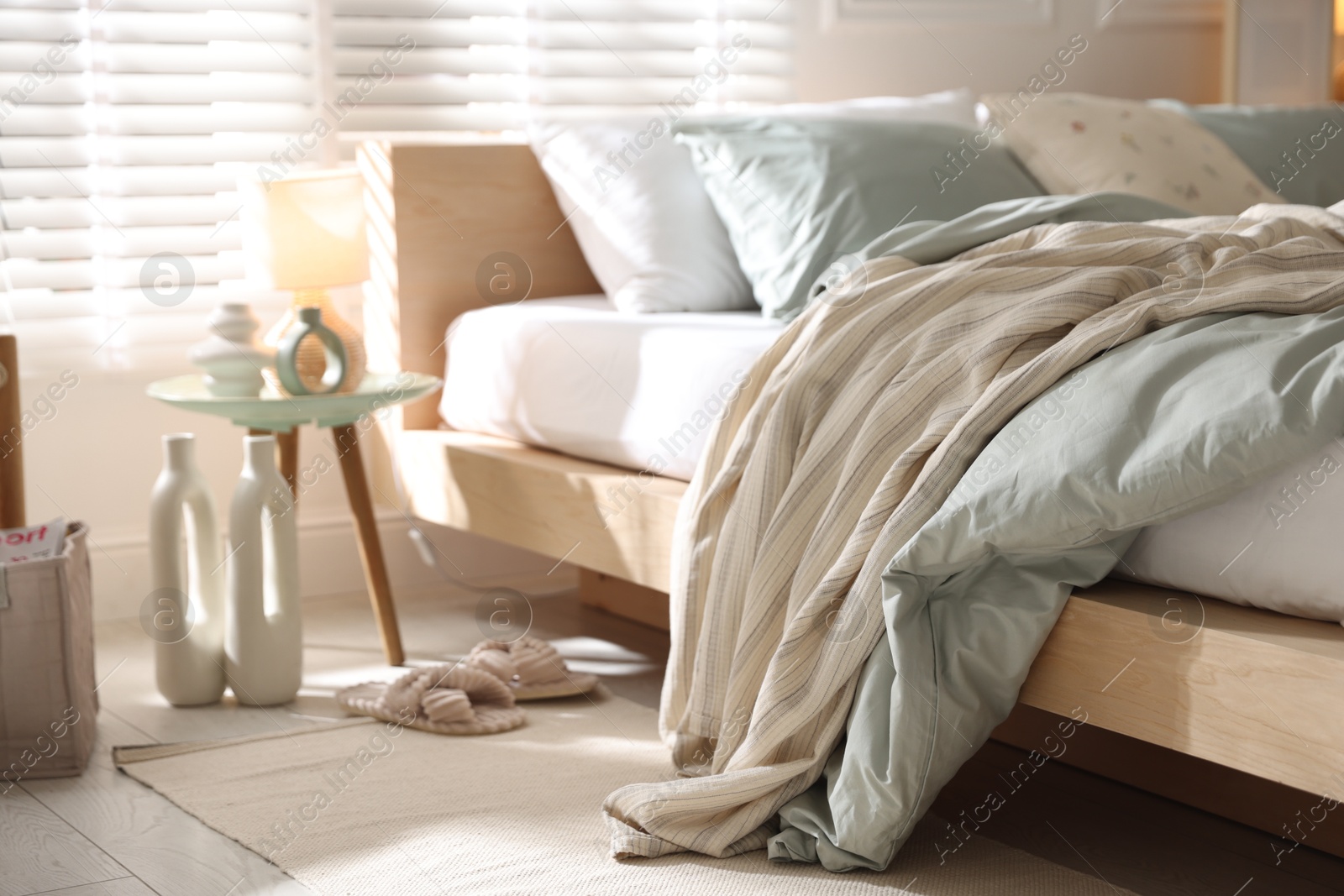 Comfortable bed with soft linens, lamp and decor in stylish room, closeup. Home textile Photo of Comfortable bed with soft linens, lamp and decor in stylish room, closeup. Home textile