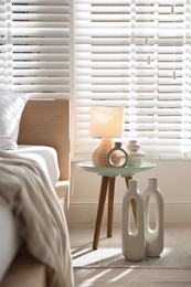 Photo of Bedside table with decor and lamp near bed in stylish bedroom. Interior design
