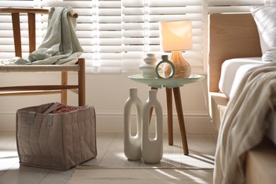 Photo of Bedside table with decor and lamp near bed in stylish bedroom. Interior design