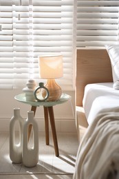 Photo of Bedside table with decor and lamp near bed in stylish bedroom. Interior design