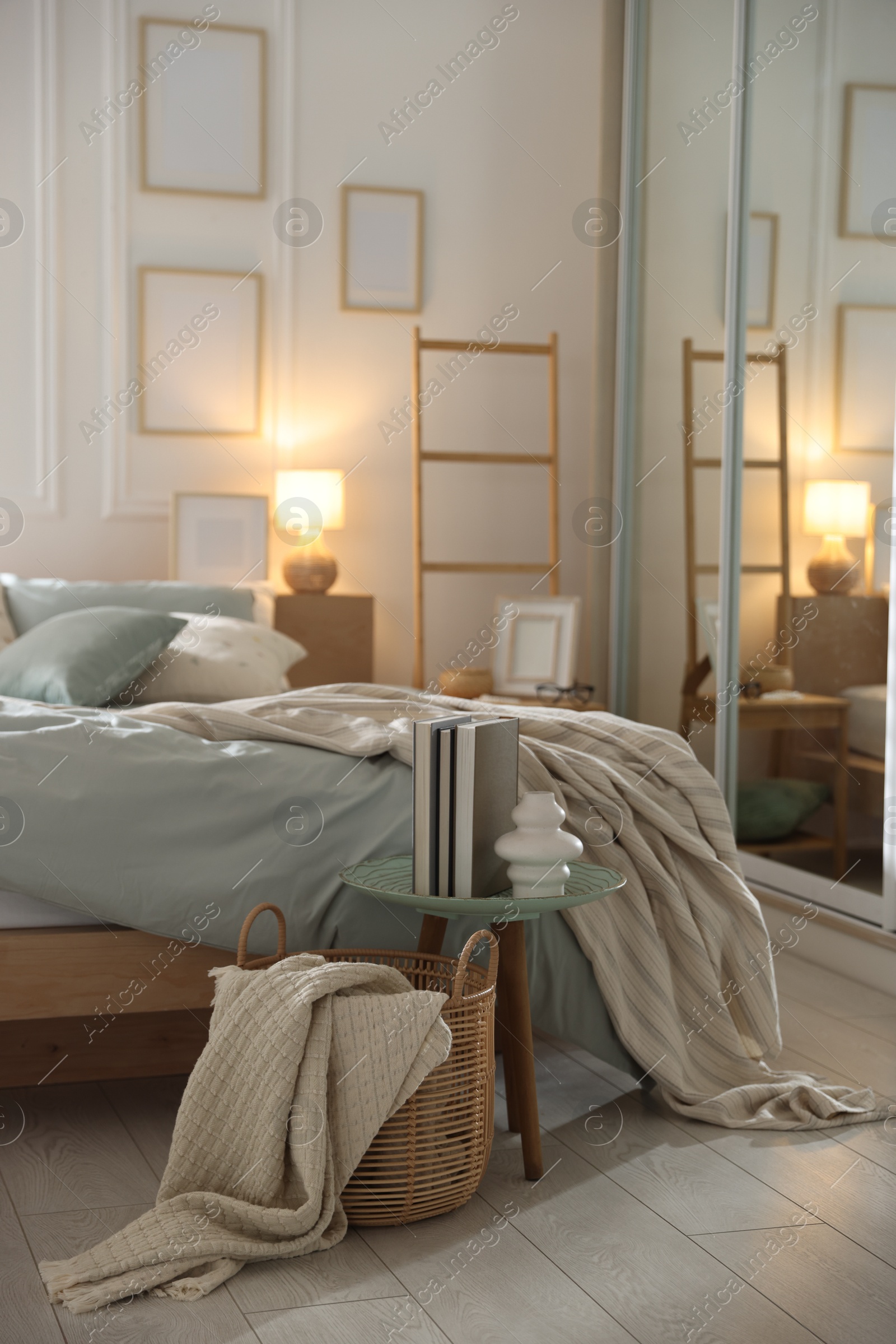 Comfortable bed with soft linens, lamp and decor in stylish room. Home textile Photo of Comfortable bed with soft linens, lamp and decor in stylish room. Home textile