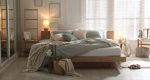 Photo of Comfortable bed with soft linens, lamp and decor in stylish room. Home textile