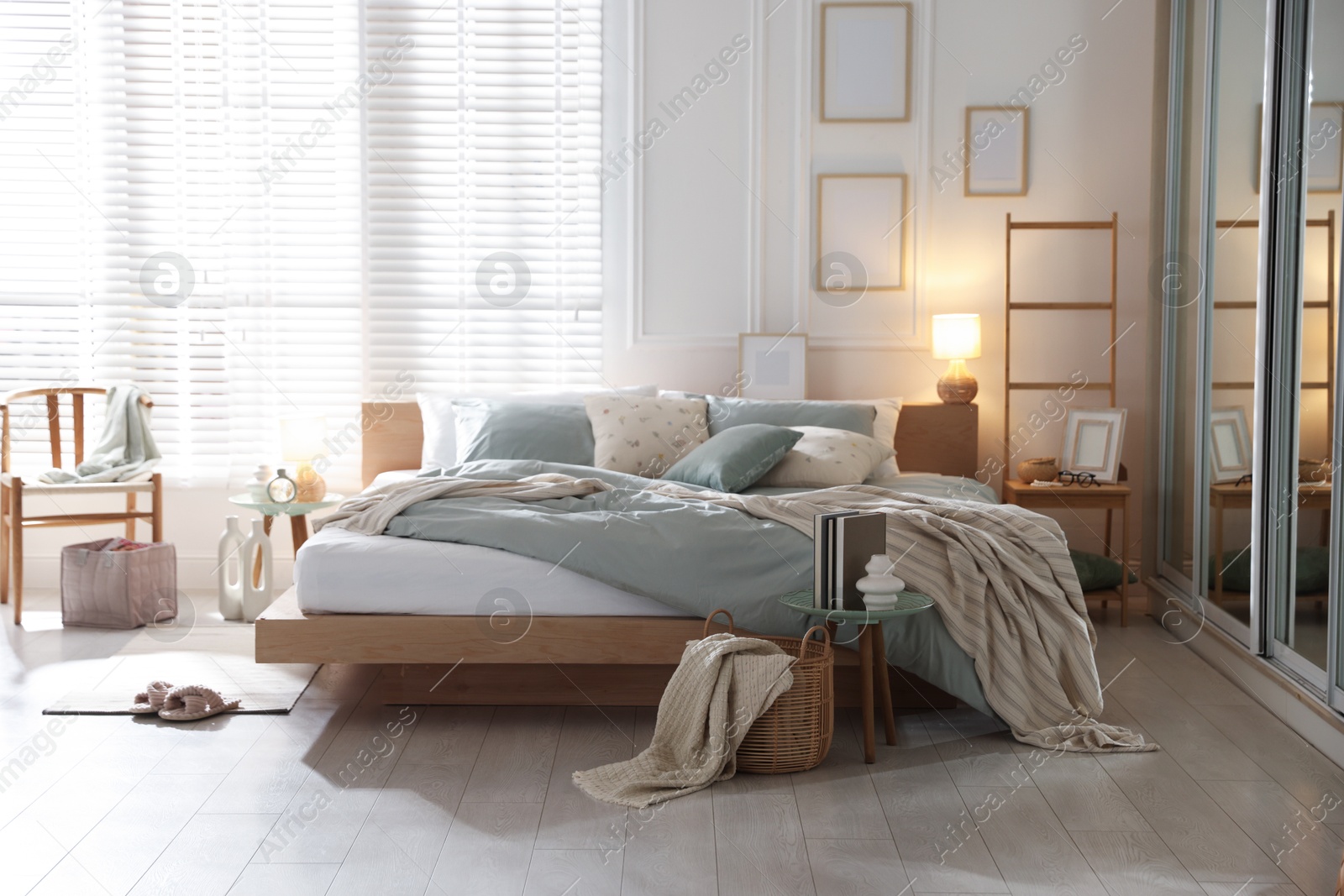 Comfortable bed with soft linens, lamp and decor in stylish room. Home textile Photo of Comfortable bed with soft linens, lamp and decor in stylish room. Home textile