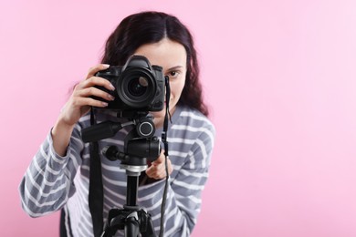 Photo of Woman with professional video camera on pink background, space for text