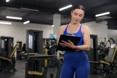 Photo of Professional personal trainer with clipboard in gym. Space for text