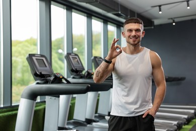 Photo of Personal trainer showing OK gesture in sport center. Space for text