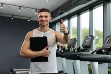 Photo of Personal trainer with clipboard showing thumbs up in sport center