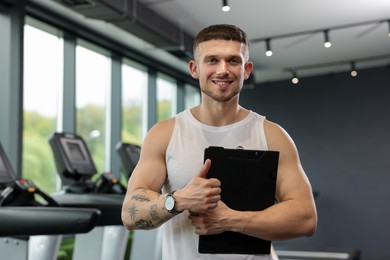Photo of Personal trainer with clipboard showing thumbs up in sport center