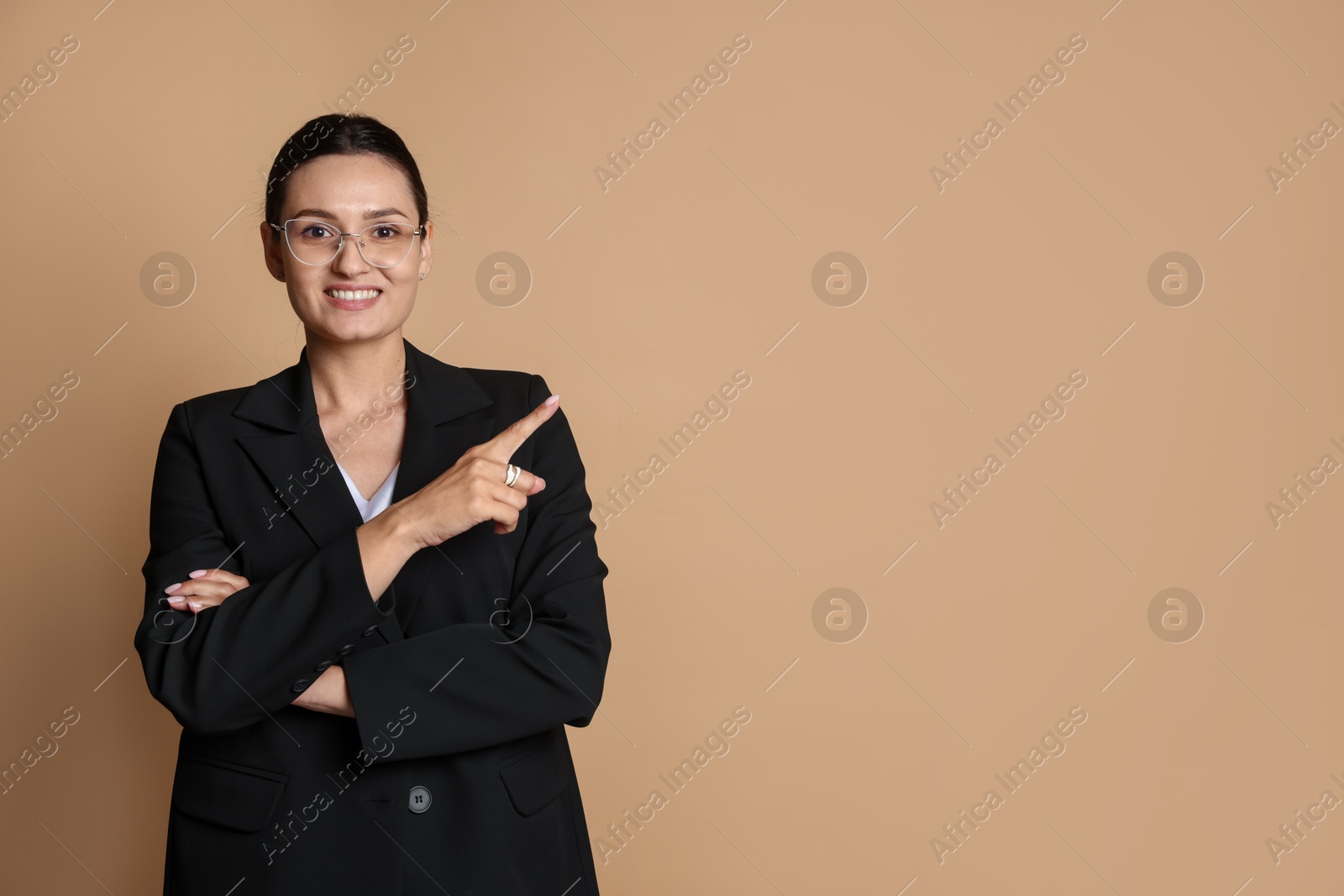 Confident business woman in suit pointing at something on beige background. Space for text Photo of Confident business woman in suit pointing at something on beige background. Space for text