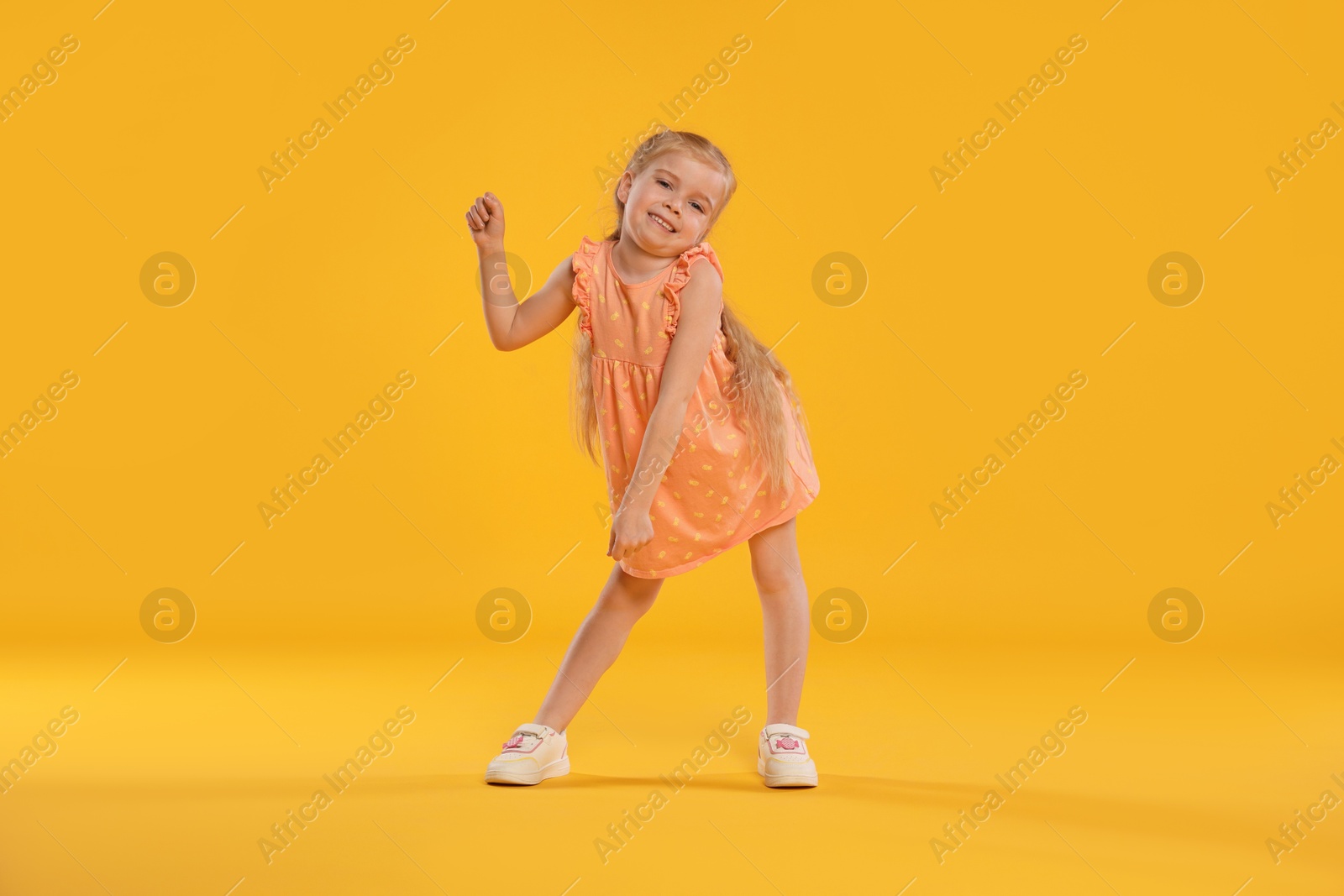 Cute little girl dancing on orange background Photo of Cute little girl dancing on orange background