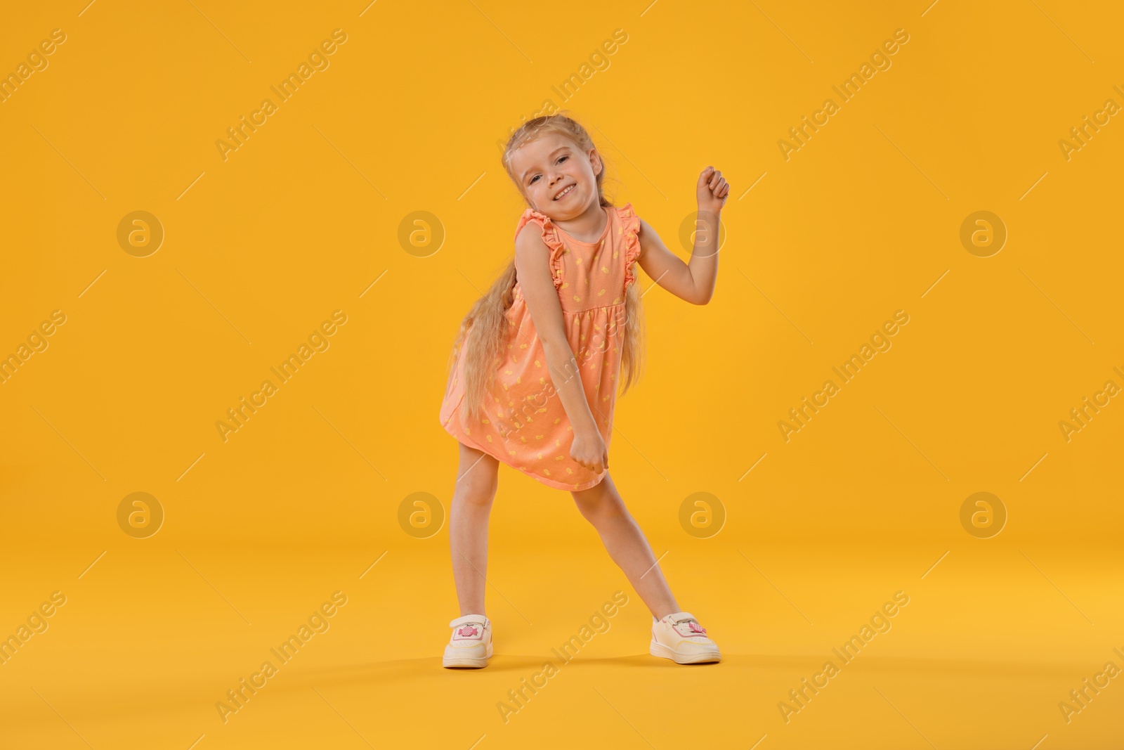 Cute little girl dancing on orange background Photo of Cute little girl dancing on orange background