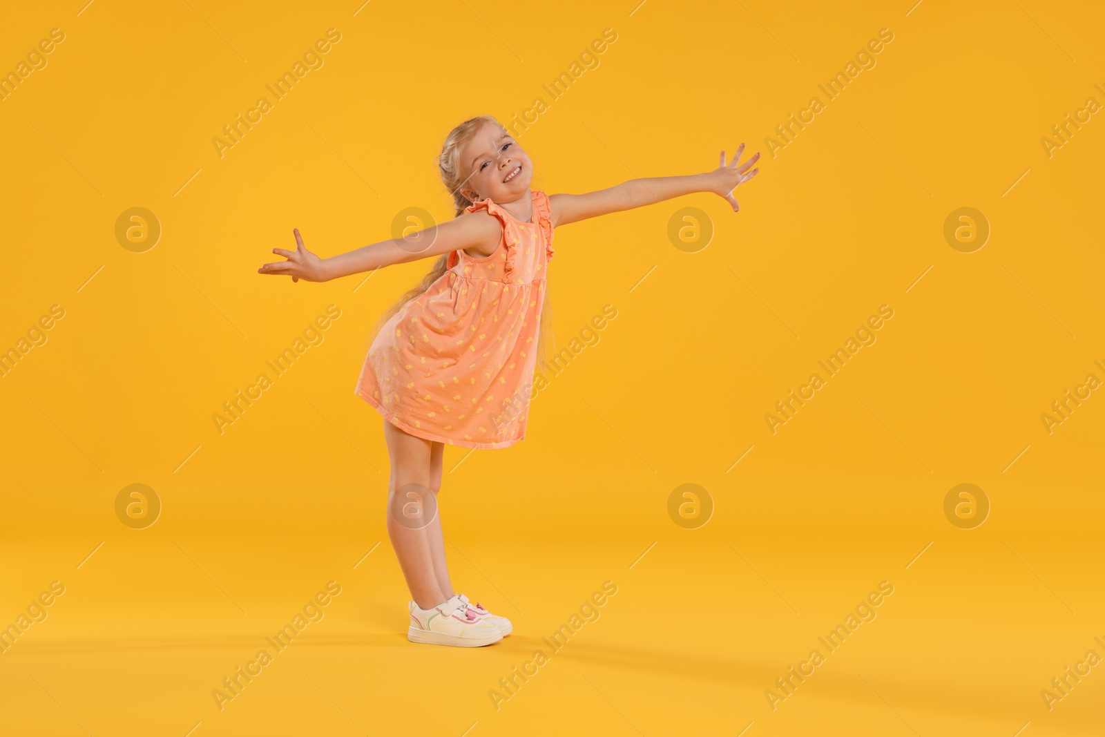 Cute little girl dancing on orange background Photo of Cute little girl dancing on orange background