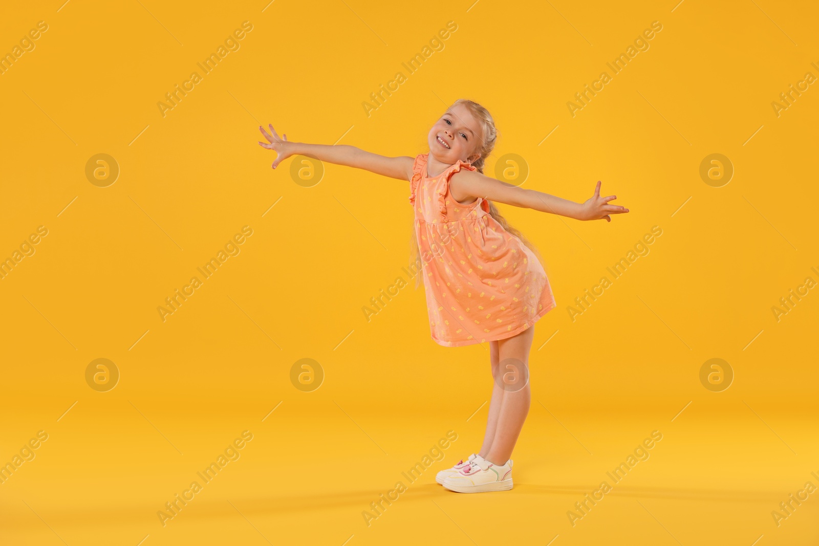 Cute little girl dancing on orange background Photo of Cute little girl dancing on orange background