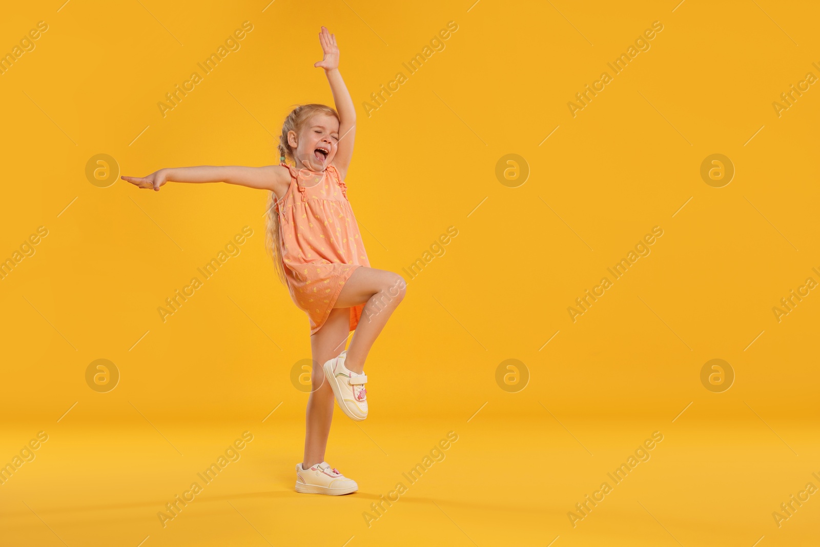 Cute little girl dancing on orange background, space for text Photo of Cute little girl dancing on orange background, space for text