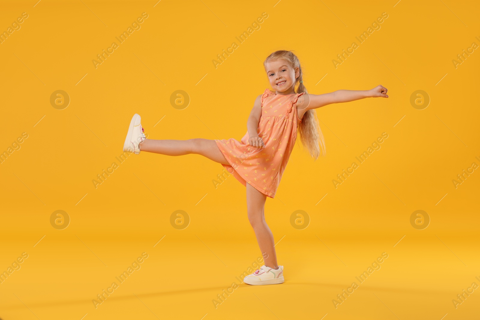 Cute little girl dancing on orange background Photo of Cute little girl dancing on orange background