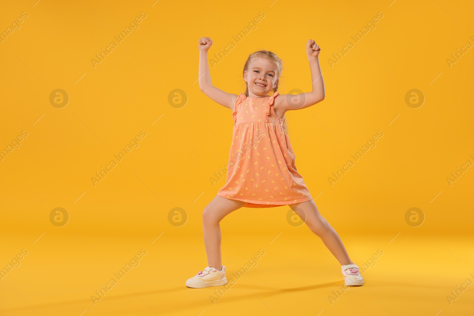 Cute little girl dancing on orange background Photo of Cute little girl dancing on orange background
