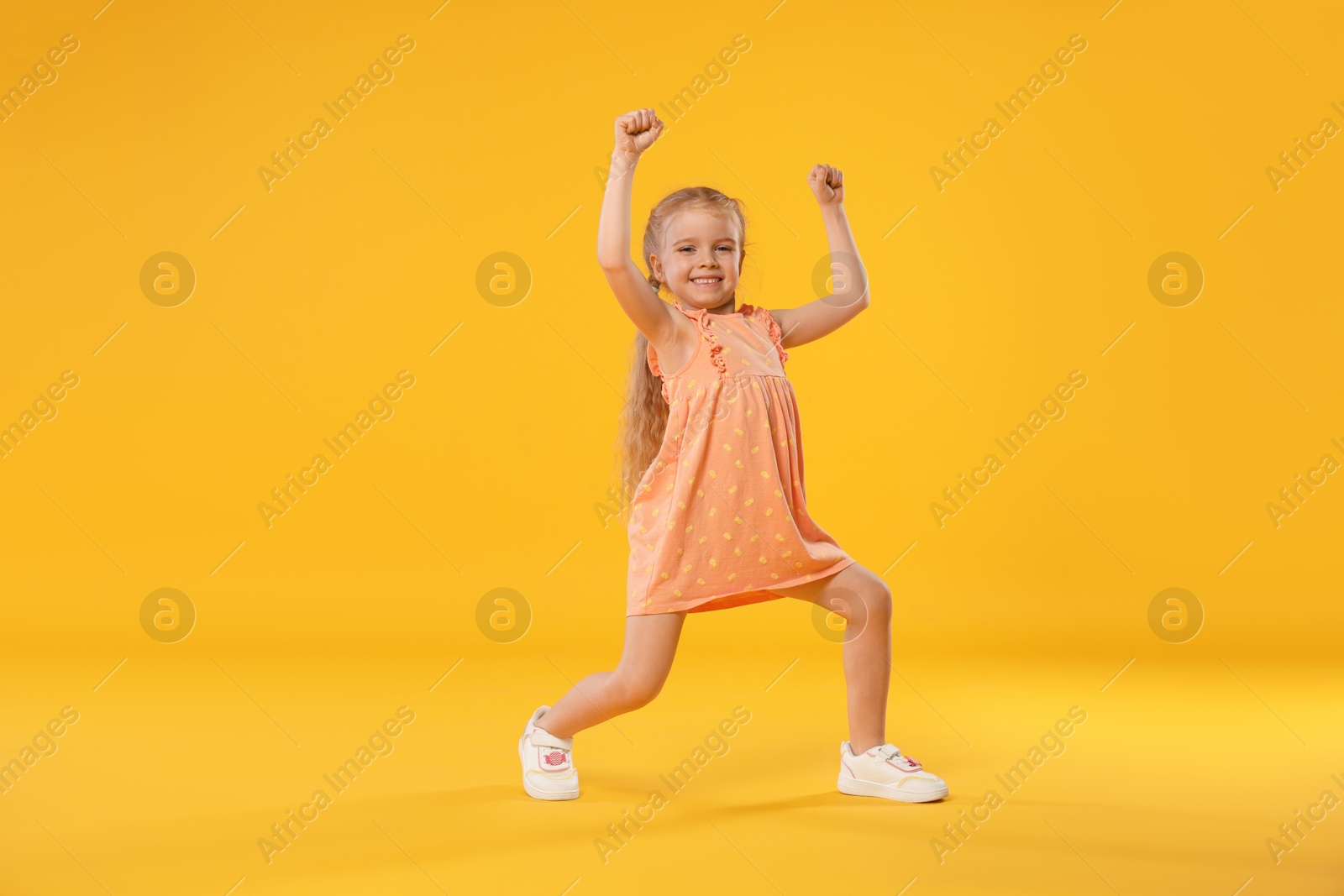 Cute little girl dancing on orange background Photo of Cute little girl dancing on orange background