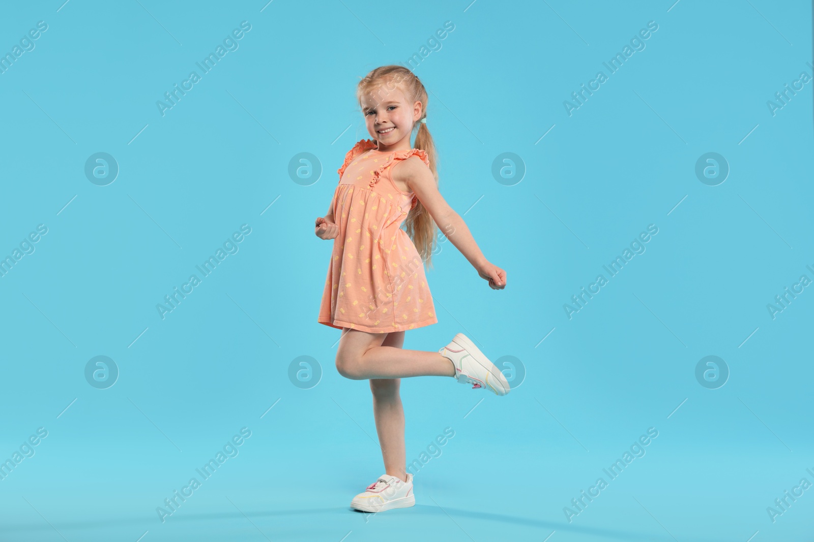 Cute little girl dancing on light blue background Photo of Cute little girl dancing on light blue background