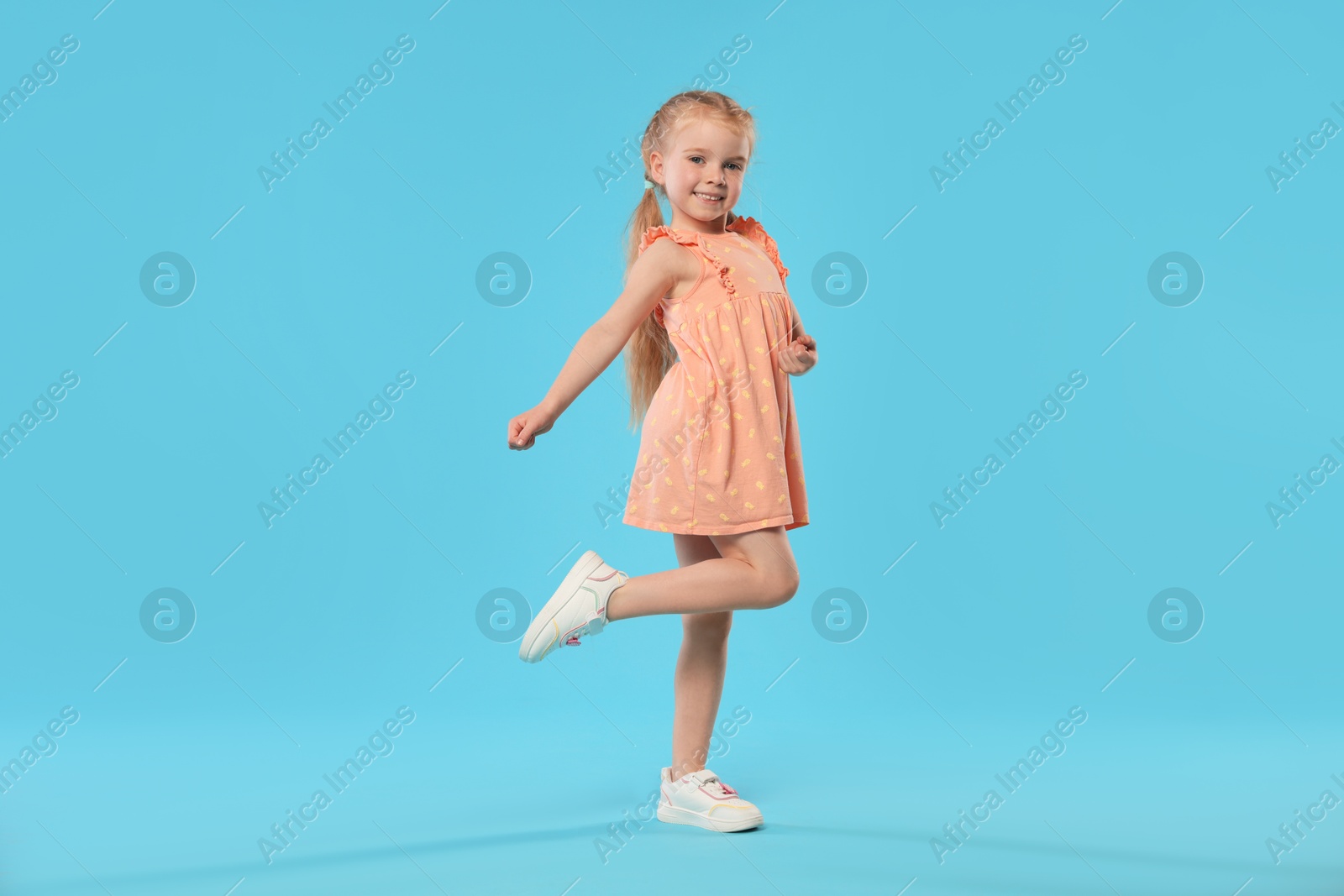 Cute little girl dancing on light blue background Photo of Cute little girl dancing on light blue background