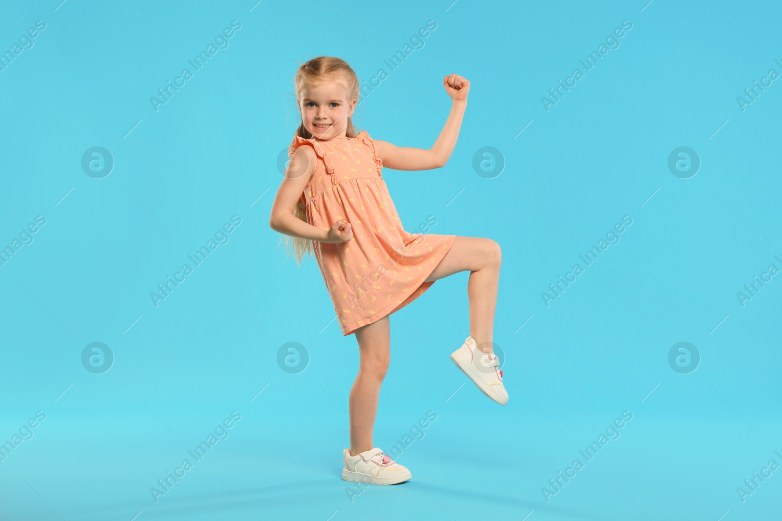 Cute little girl dancing on light blue background Photo of Cute little girl dancing on light blue background
