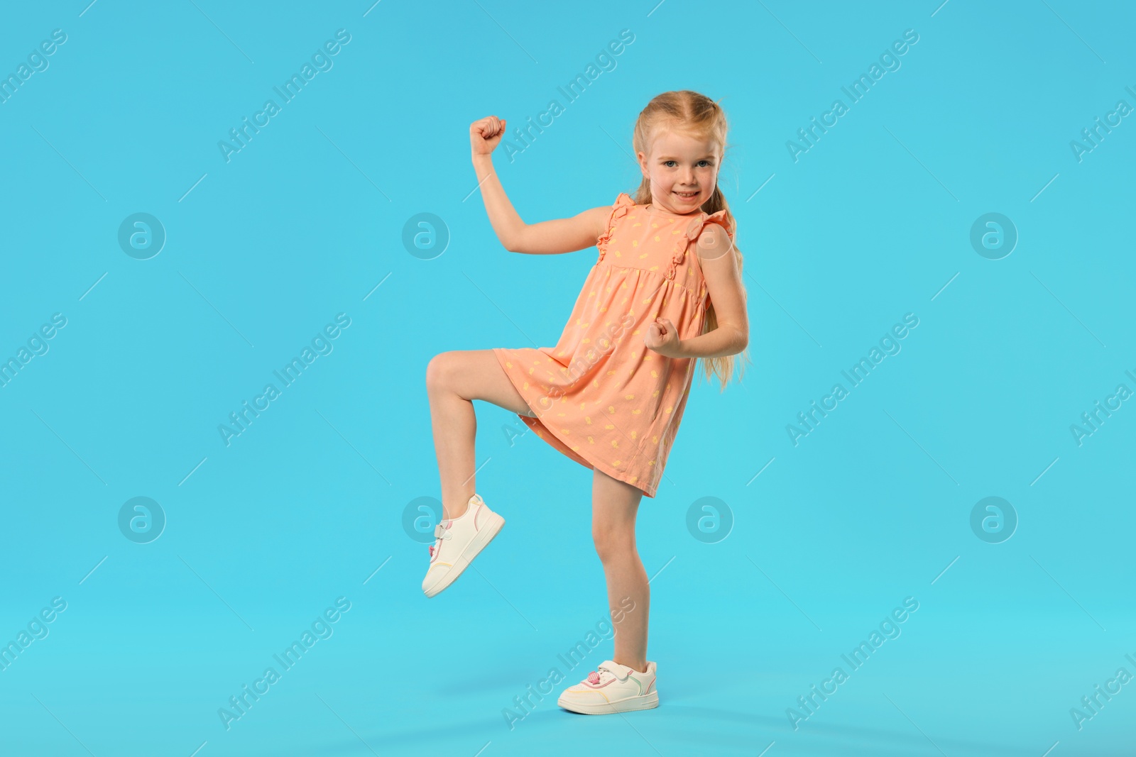 Cute little girl dancing on light blue background Photo of Cute little girl dancing on light blue background