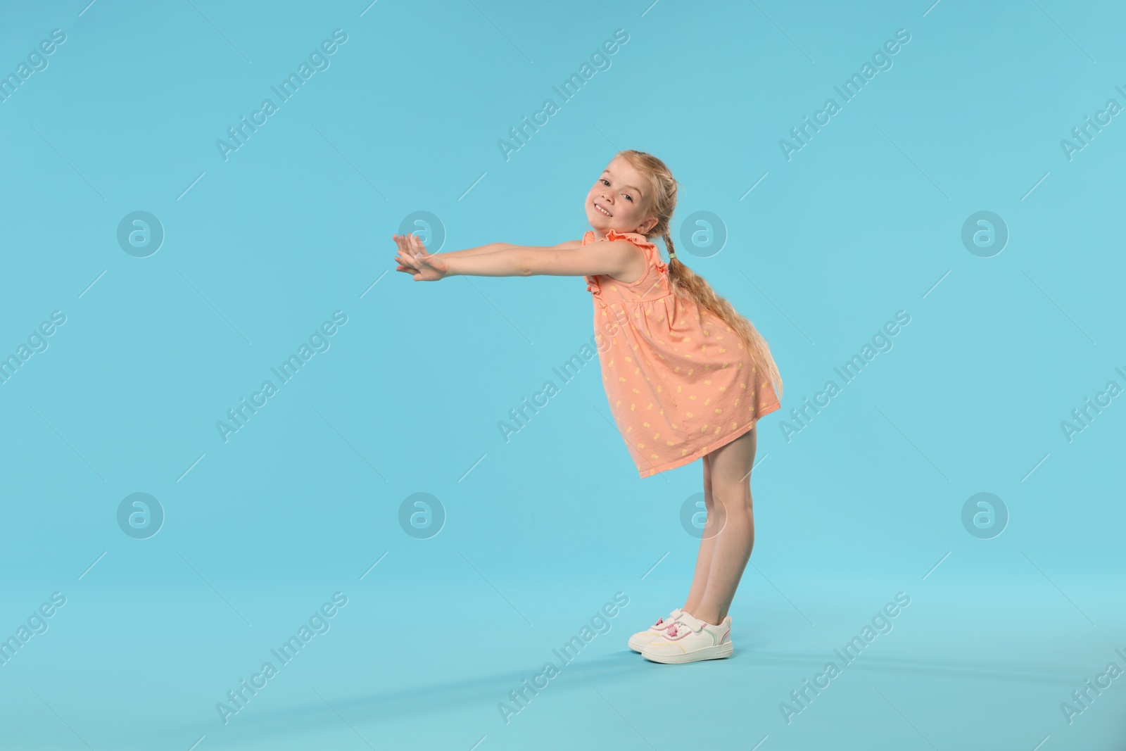 Cute little girl dancing on light blue background Photo of Cute little girl dancing on light blue background
