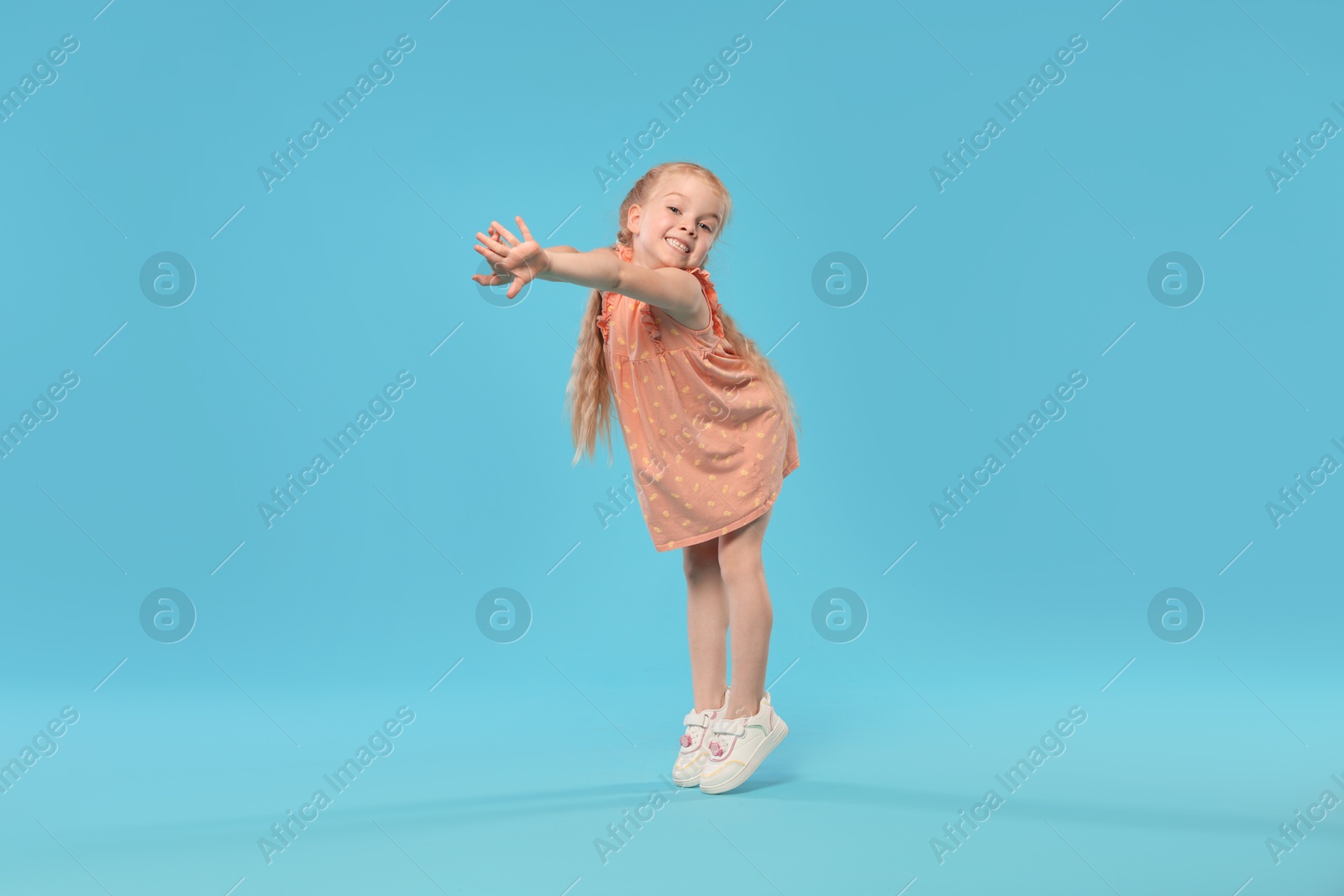 Cute little girl dancing on light blue background Photo of Cute little girl dancing on light blue background