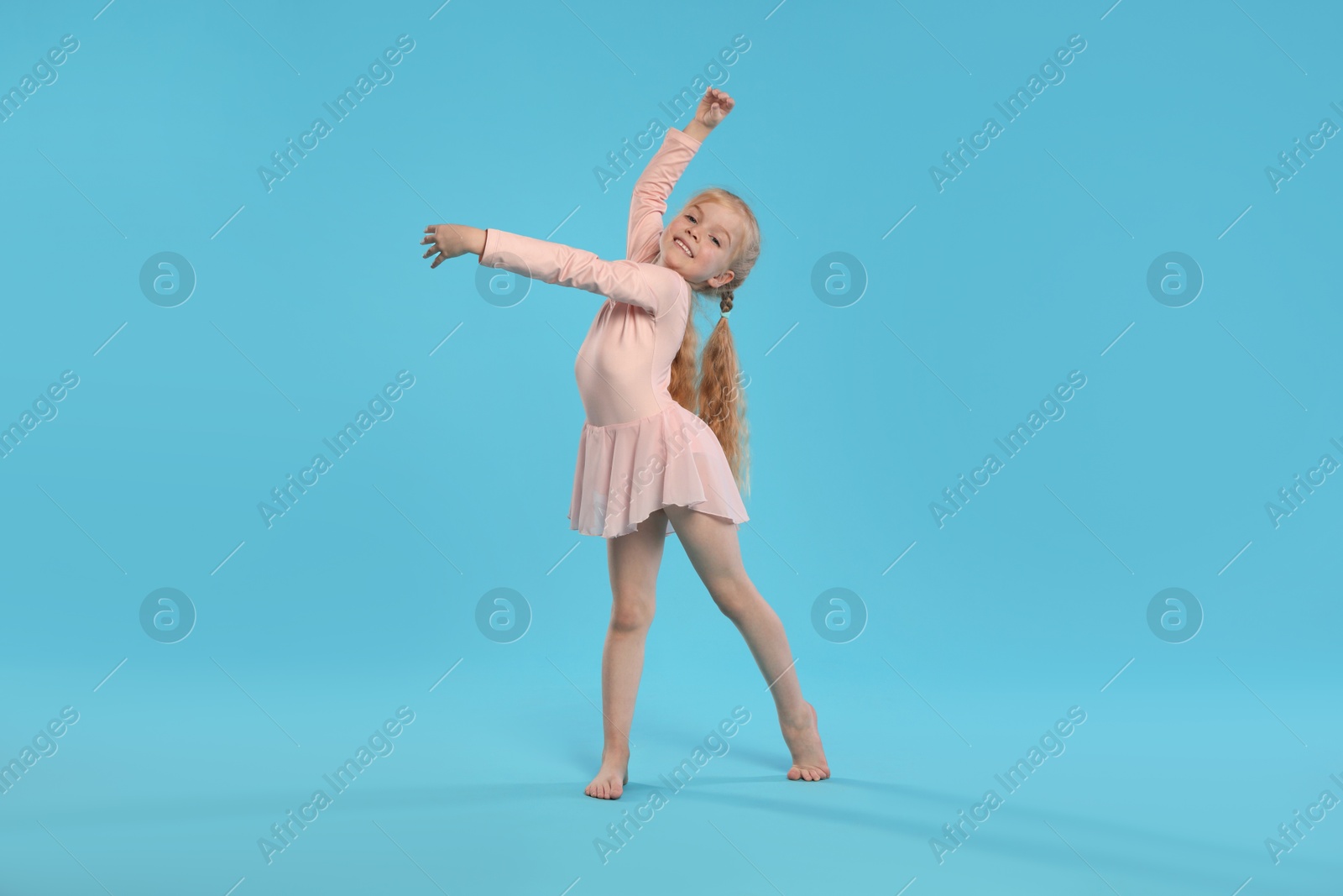 Cute little girl dancing on light blue background Photo of Cute little girl dancing on light blue background