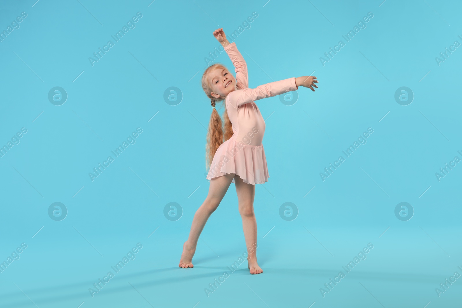 Photo of Cute little girl dancing on light blue background