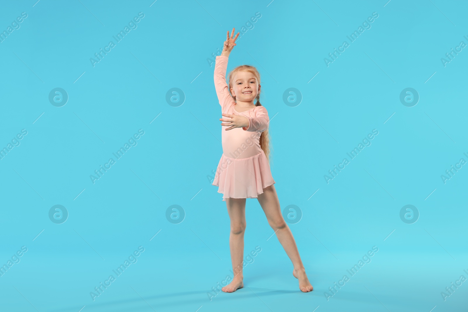 Cute little girl dancing on light blue background Photo of Cute little girl dancing on light blue background