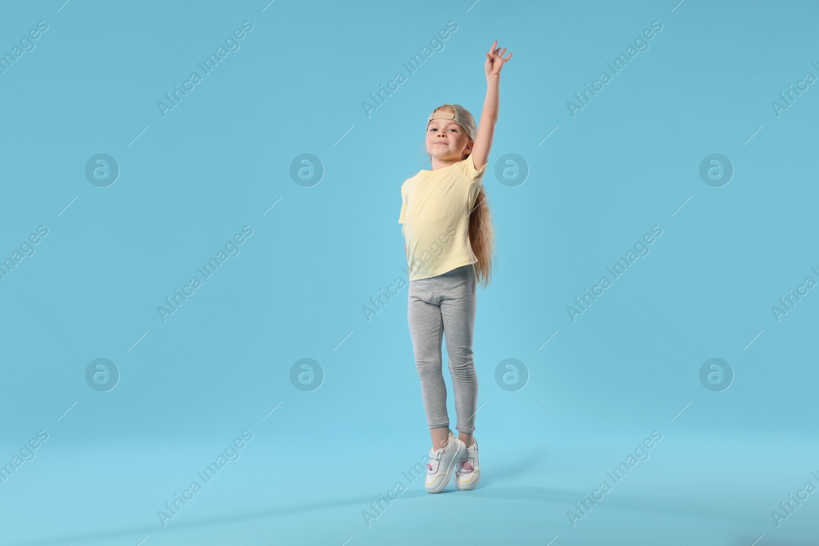 Cute little girl dancing on light blue background Photo of Cute little girl dancing on light blue background