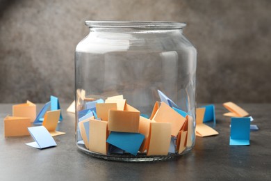 Photo of Jar with colorful pieces of paper on grey table, closeup
