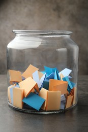 Photo of Jar with colorful pieces of paper on grey table, closeup