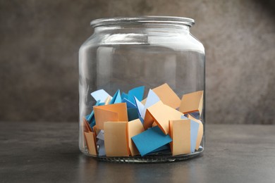 Photo of Jar with colorful pieces of paper on grey table, closeup