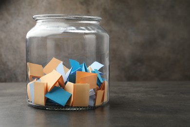 Photo of Jar with colorful pieces of paper on grey table, closeup. Space for text