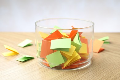 Photo of Jar with colorful pieces of paper on wooden table against light background, closeup