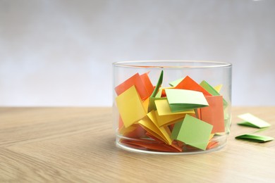 Photo of Jar with colorful pieces of paper on wooden table against light background, closeup. Space for text