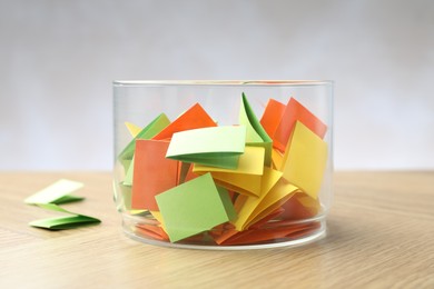 Photo of Jar with colorful pieces of paper on wooden table against light background, closeup