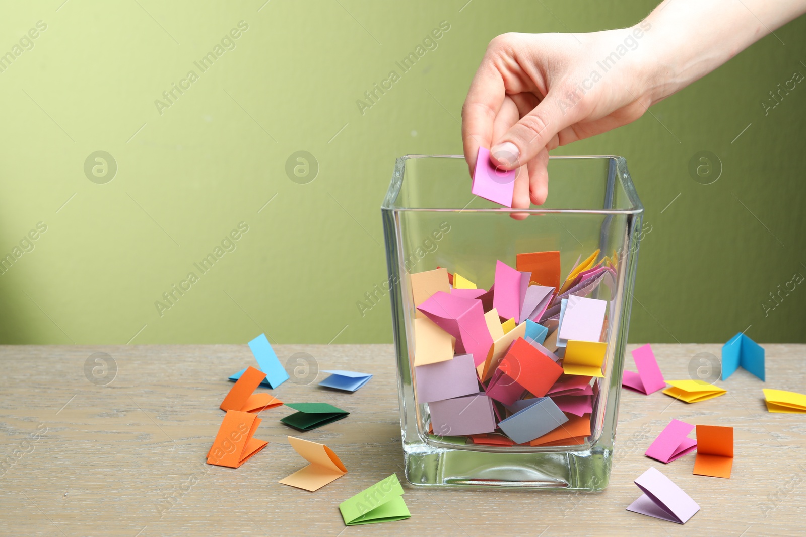 Photo of Woman taking paper with message out of jar at wooden table, closeup