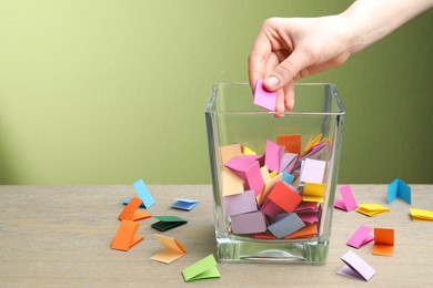 Photo of Woman taking paper with message out of jar at wooden table, closeup