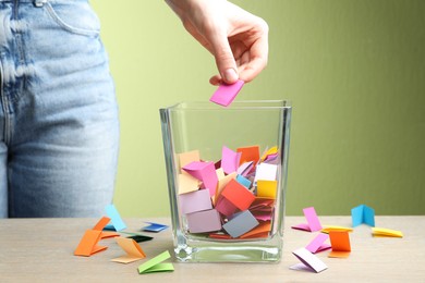 Photo of Woman taking paper with message out of jar at wooden table, closeup