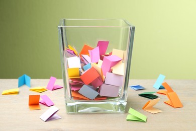 Photo of Jar with colorful pieces of paper on wooden table against green background, closeup