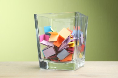 Photo of Jar with colorful pieces of paper on wooden table against green background, closeup