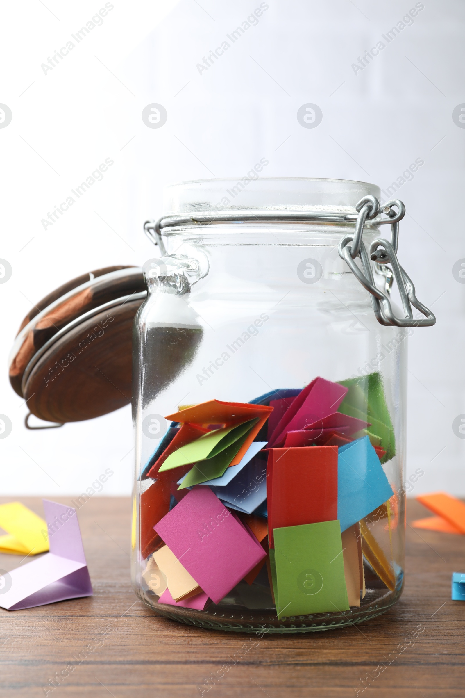 Jar with colorful pieces of paper on wooden table near white brick wall, closeup Photo of Jar with colorful pieces of paper on wooden table near white brick wall, closeup