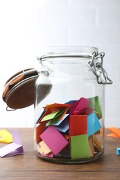 Photo of Jar with colorful pieces of paper on wooden table near white brick wall, closeup