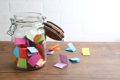 Photo of Jar with colorful pieces of paper on wooden table near white brick wall. Space for text